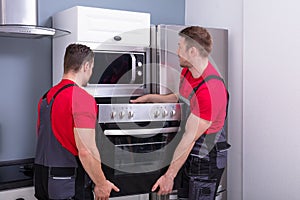 Young Male Worker Placing Modern Oven In Kitchen