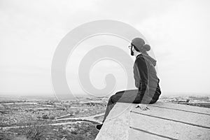 Side view unidentified young man in casual clothes and glasses sits on the high rock and looks at beautiful desert