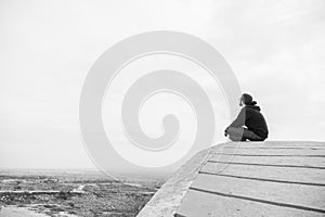 Side view unidentified young man in casual clothes and glasses sits on the high rock and looks at beautiful desert