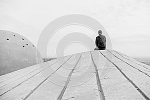 Side view unidentified young man in casual clothes and glasses sits on the high rock and looks at beautiful desert