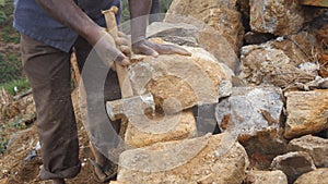 Side view of unrecognizable indian man cutting a block of granite with hammer in botanical garden. Adult human hitting
