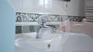 Side view of unrecognizable little girl washing hands with liquid soap and water. Diligent child cleaning palms