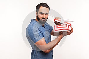 Side view unsatisfied displeased man holding in hands unpacked gift box, frustrated with content, bad present