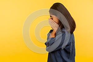 Side view of upset dramatic girl in denim shirt crying with sorrow, wiping tears, feeling lonely hopeless