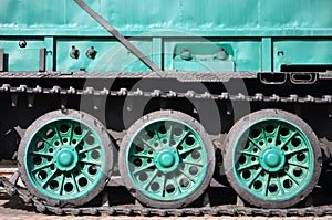 Side view of the vehicle on a caterpillar track with black tracks and green wheels and a side metal wal