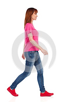 Side View Of Walking Young Woman In Pink Shirt, Jeans And Red Sneakers