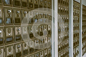Side view of wall of aged brown metal post office mail boxes with silver combination star locks and glass windows