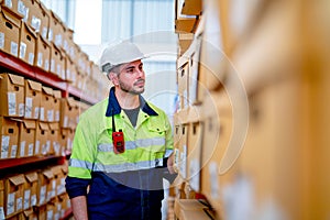 Side view warehouse worker man stand in front of the shelves and look to product box in workplace