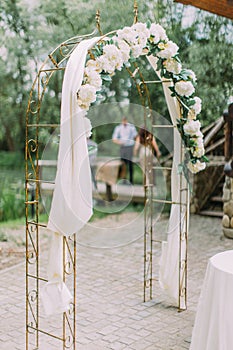 The side view of the wedding arch decorated with white flowers.