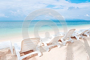 Side view of white beach chairs on white sand tropical beach wit