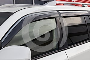 Side view of a white Japanese car in the body of a SUV with wind visors on windows in a parking after being washed ready for sale