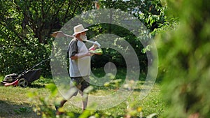 Side view wide shot of confident senior man with shovel on shoulder and harvest walking in slow motion in sunny garden