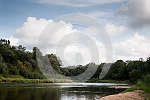 Side view on wide still river in forest in summer day with blue sky and clouds