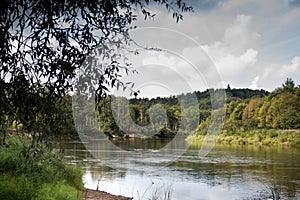 Side view on wide still river in forest in summer day with blue sky and clouds