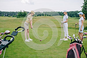 side view of woman in cap playing golf while friends standing near by