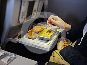 Side view of woman eating delicious meal in modern aircraft economy business