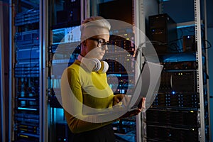 Side view of woman engineer working on laptop at network equipment