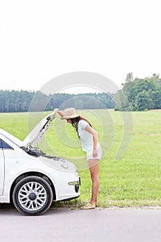 Side view of woman examining broken down car on country road