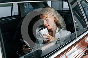 Side view. Woman in formal clothes is indoors in the autosalon