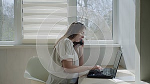 Side view of woman freelanser using laptop notebook and talking on phone at home.