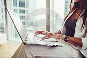 Side view of woman holding laptop on her lap working in office