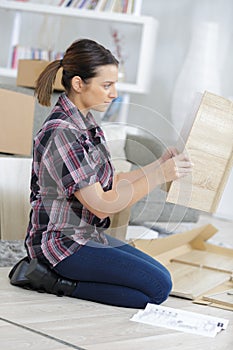 Side view woman knelt on floor assembling furniture