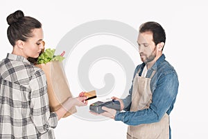 side view of woman with paper package with food giving credit card to shop assistant with cardkey reader