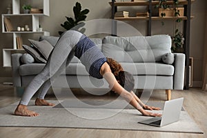 Side view woman practicing yoga online, doing Downward facing dog exercise