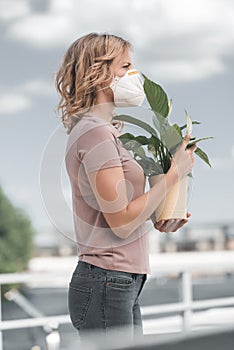 side view of woman in protective mask holding potted plant on bridge air