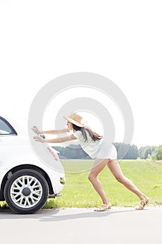 Side view of woman pushing broken down car on country road