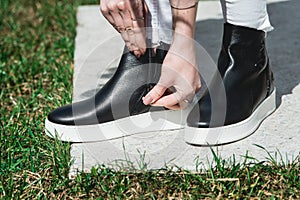 Side View Of Woman`s Black Leather Ankle Boots. Outdoor Shot Over White Stone in park