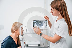 Side view. Woman`s vision is tested by clinic worker that using special device