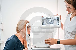 Side view. Woman`s vision is tested by clinic worker that using special device