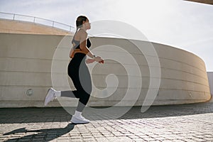 Side view of woman in sportswear is running on modern buildings background. Active lifestyle concept