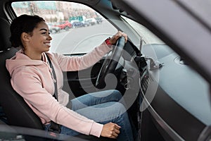 Side view of woman taxi driver sitting in transport, holding steering wheel and looking on road