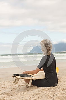 Side view of woman in wetsuit sitting with surfboard