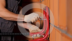 Side view of a worker hanging heavy metal object on the wall made of ceramic blocks. Stock footage. Close up of male