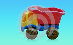 side view yellow and red and blue and green plastic truck toy on gradient blue and green background, object, toy, play, banner,