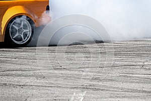side view of yellow sport car drifting on gray speed tarmac track with smoke coming out of the back tire wheel