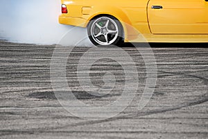 side view of yellow sport car drifting on gray speed tarmac track with smoke coming out of the back tire wheel