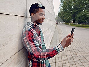 Side view young african man using or taking selfie picture by phone on city street