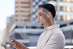 Side view of a young Asian man typing on his cellphone in the city