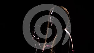 Side view of a young attractive woman who sings sexually into a vintage microphone. Shot in a dark studio with back