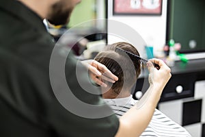 Side view of young bearded man getting beard haircut at hairdresser while sitting in chair at barbershop