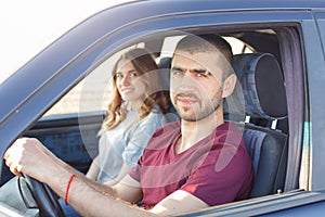 Side view of young beautiful couple has trip in car, look at camera, being in their automobile, enjoy high speed. Family cover
