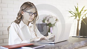 Side view of a young beautiful woman wearing glasses typing at her laptop in office.