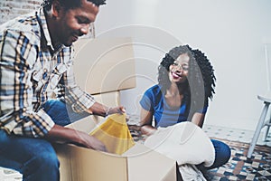 Side view of young black american african couple with moving boxes in new apartment.Cheerful couple sitting in empty new