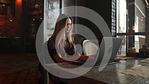 Side view. Young business woman sitting at table and taking notes in notebook.On table is laptop, smartphone and cup of