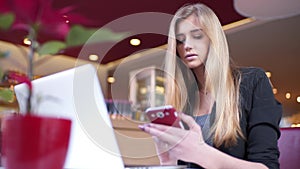 Side view. Young business woman sitting at table and taking notes in notebook.On table is laptop, smartphone and cup of