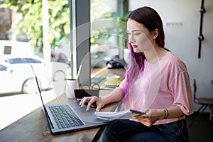 Side view of young businesswoman sitting at table in coffee shop. On table cup of coffee and laptop. In background white